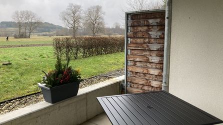 Terrasse mit schwarzem Tisch, Blumenkasten und Blick auf Feld mit kahlen Bäumen
