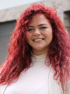 Person mit roten lockigen Haaren lächelnd vor Hausfassade