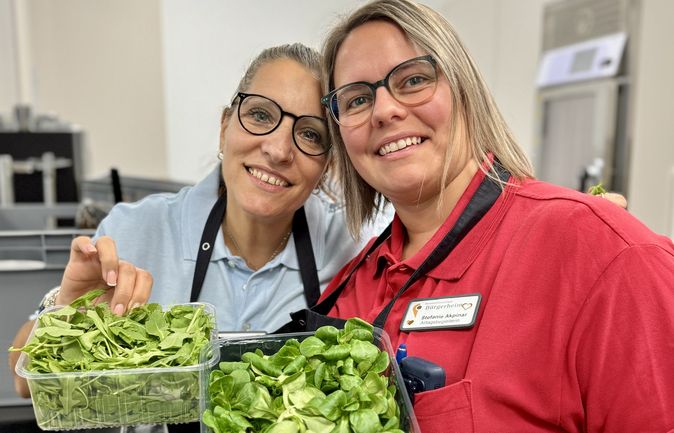Zwei lächelnde Mitarbeitende beim Koch-Event mit Schüsseln frischer Salate