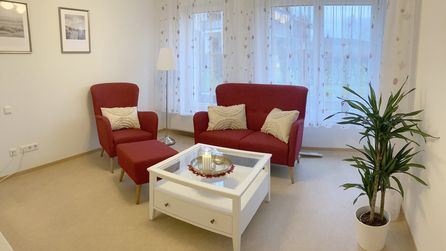 Wohnzimmer mit roten Sesseln, weißem Couchtisch und grüner Pflanze